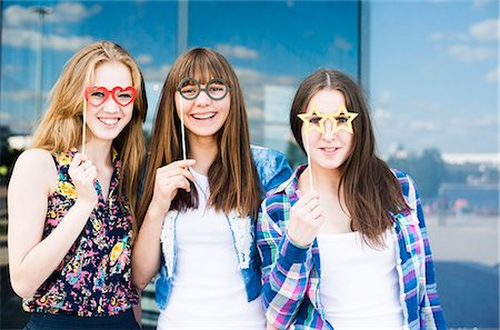 Portrait of three young women holding up spectacle costume masks Stock Photo - Premium Royalty-Free, Code: 649-07736865