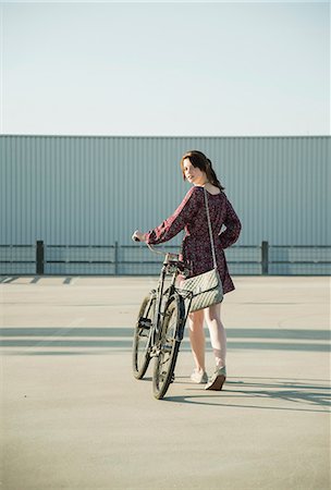 empuje - Young woman looking back whilst pushing bicycle in empty parking lot Foto de stock - Sin royalties Premium, Código: 649-07736955