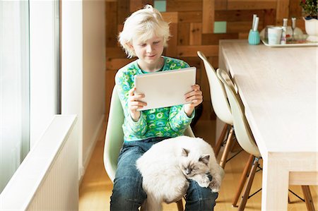 Boy with cat on his lap using digital tablet in kitchen Stock Photo - Premium Royalty-Free, Code: 649-07737034