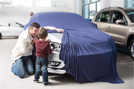 Mid adult man uncovering new car for son in car dealership Stock Photo - Premium Royalty-Free, Code: 649-07761175