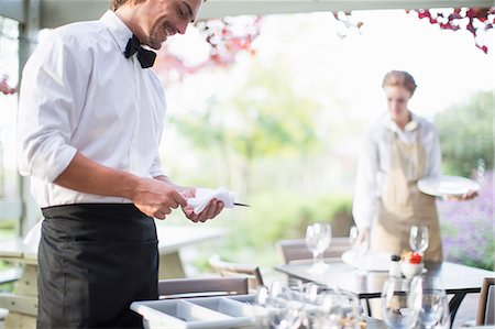 Waiter polishing cutlery with napkin in patio restaurant Photographie de stock - Premium Libres de Droits, Code: 649-07761231