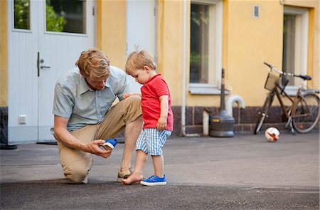 Father giving toddler son a hand to put on trainer in garden Foto de stock - Sin royalties Premium, Código: 649-07761262