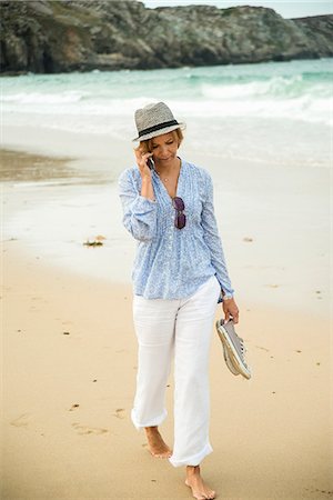 Mature woman chatting on smartphone whilst strolling on beach, Camaret-sur-mer, Brittany, France Photographie de stock - Premium Libres de Droits, Code: 649-07804021