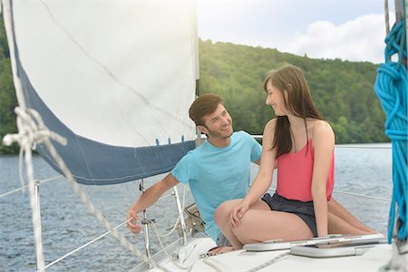 Young couple sailing on sunlit yacht over lake, smiling Stock Photo - Premium Royalty-Free, Code: 649-07804404