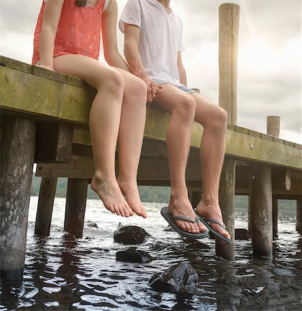 people sitting on dock - Young couple holding hands together and sitting on edge of jetty over lake Stock Photo - Premium Royalty-Free, Code: 649-07804411