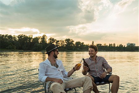 The boy is sitting on a folding chair on the shore of a lake or river.  Recreation, weekends, tourism. Rear view - a Royalty Free Stock Photo from  Photocase