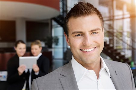 simsearch:649-07804776,k - Smiling businessman, colleagues in background using digital tablet Stock Photo - Premium Royalty-Free, Code: 649-07804776