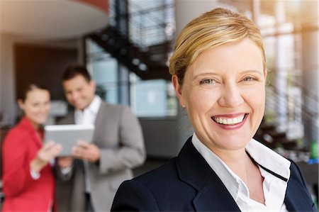 simsearch:614-07487004,k - Smiling businesswoman, colleagues in background using digital tablet Stock Photo - Premium Royalty-Free, Code: 649-07804777