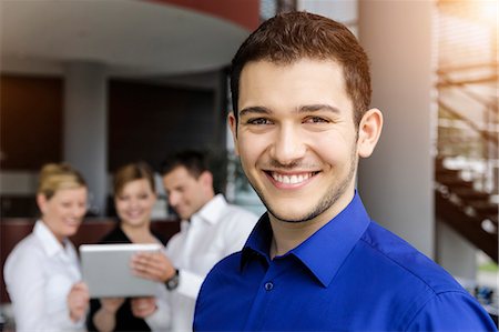 simsearch:649-07804776,k - Smiling businessman, colleagues in background using digital tablet Stock Photo - Premium Royalty-Free, Code: 649-07804778