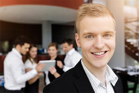 simsearch:649-07804776,k - Smiling businessman, colleagues in background using digital tablet Stock Photo - Premium Royalty-Free, Code: 649-07804781