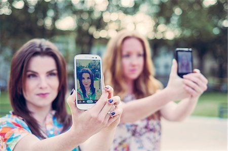 Two young female friends taking selfie on smartphones in unison Stock Photo - Premium Royalty-Free, Code: 649-07804828