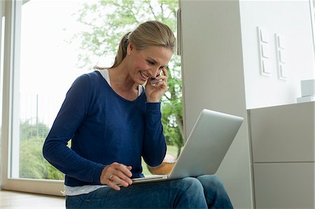 Mature woman using laptop on cell phone Stock Photo - Premium Royalty-Free, Code: 649-07804994