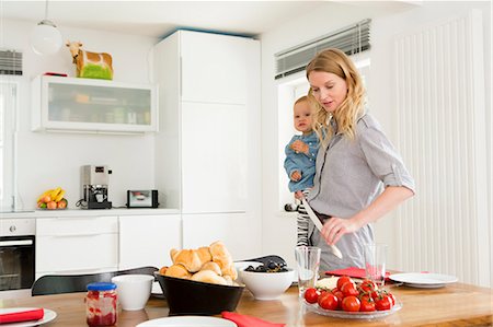 Mother setting kitchen table while holding baby daughter Photographie de stock - Premium Libres de Droits, Code: 649-07805099