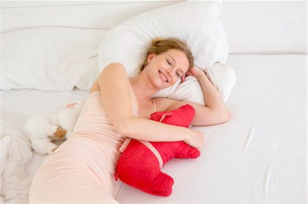 pig - Mid adult woman lying on bed holding soft toy Stock Photo - Premium Royalty-Free, Code: 649-07805127