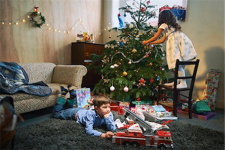 Girl arranging christmas tree whilst brother plays with xmas gifts on sitting room floor Photographie de stock - Premium Libres de Droits, Code: 649-07803303