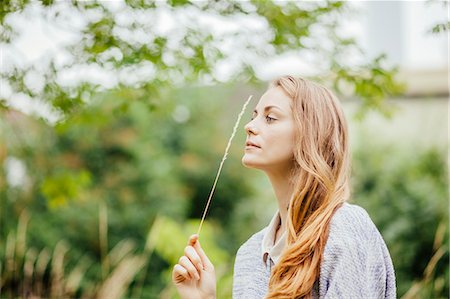 simsearch:649-07239774,k - Young woman in field holding up a stem of long grass Stock Photo - Premium Royalty-Free, Code: 649-07803347