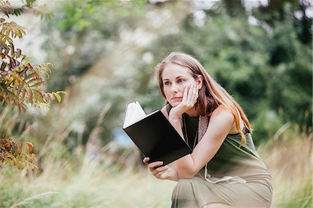 simsearch:649-06844461,k - Young woman with chin on hand reading book in field Fotografie stock - Premium Royalty-Free, Codice: 649-07803350