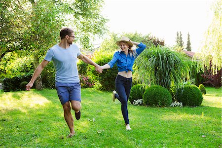 run straw hat run - Mid adult couple holding hands whilst running in garden Stock Photo - Premium Royalty-Free, Code: 649-07803449