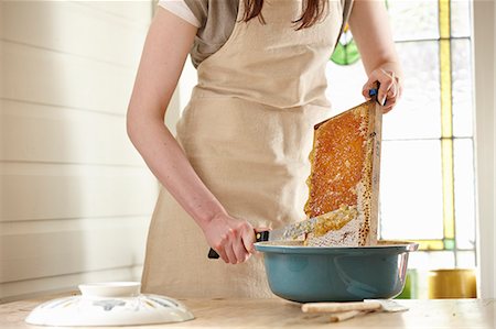 Female beekeeper in kitchen scraping "super" (honeycomb frame) Stock Photo - Premium Royalty-Free, Code: 649-07803955