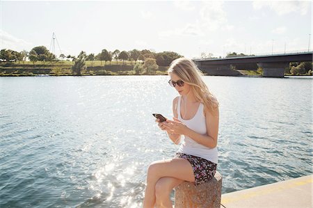 Young woman sitting at riverside texting on smartphone, Danube Island, Vienna, Austria Foto de stock - Sin royalties Premium, Código: 649-07905181