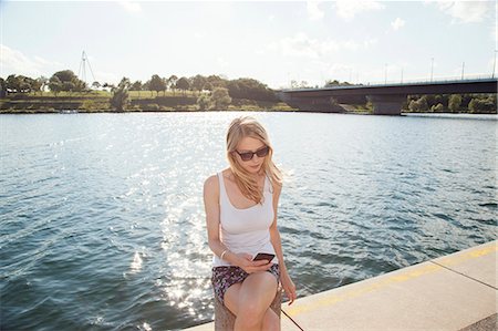 simsearch:649-07905189,k - Young woman sitting at riverside reading texts on smartphone, Danube Island, Vienna, Austria Photographie de stock - Premium Libres de Droits, Code: 649-07905183