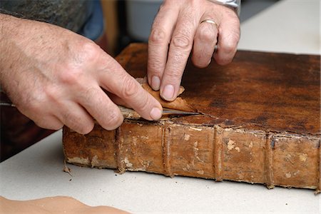 Close up of hands of senior male traditional bookbinder removing leather from book Stock Photo - Premium Royalty-Free, Code: 649-07905308