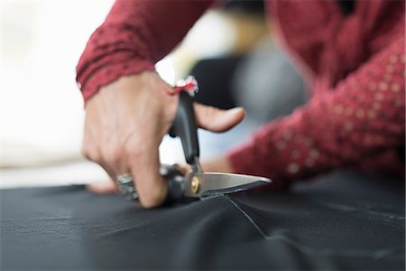 Close up of seamstress hands using scissors to cut textile at work table Stock Photo - Premium Royalty-Free, Code: 649-07905510