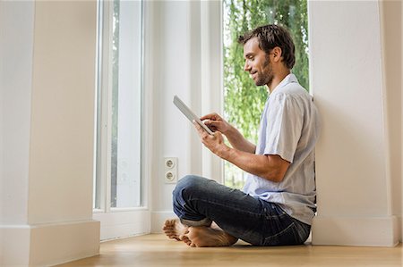 Mid adult man using touchscreen on digital tablet in sitting room Stock Photo - Premium Royalty-Free, Code: 649-08004091