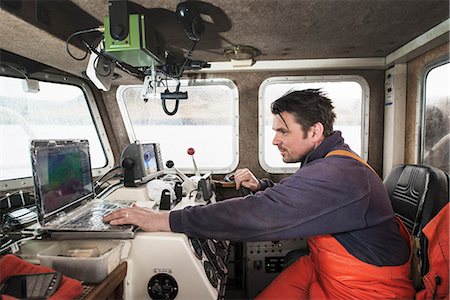 Fisherman driving fishing boat using laptop Stock Photo - Premium Royalty-Free, Code: 649-08004131