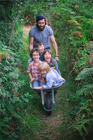 friendship, fun - Mid adult man pushing wheelbarrow with smiling boys in garden Stock Photo - Premium Royalty-Free, Code: 649-08004286