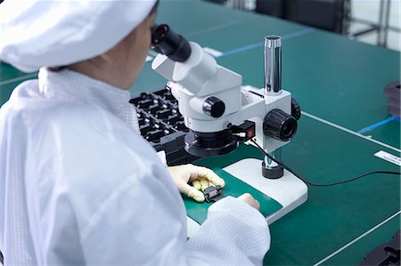 Worker using microscope in factory that specialises in creating functional circuits on flexible surfaces Photographie de stock - Premium Libres de Droits, Code: 649-08004306