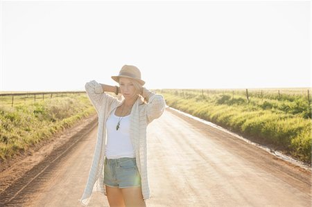 simsearch:649-08125865,k - Mid adult woman on country road, arms behind neck, looking at camera Fotografie stock - Premium Royalty-Free, Codice: 649-08003947