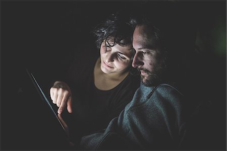 Couple sitting in dark room, looking at digital tablet Stock Photo - Premium Royalty-Free, Code: 649-08060299