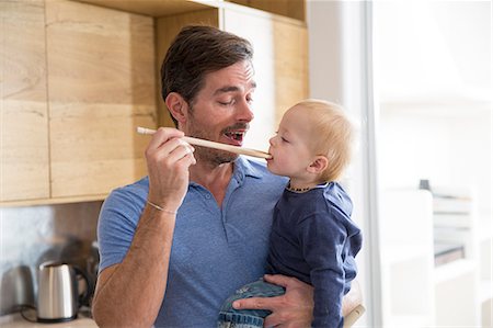 Man feeding toddler son with wooden spoon in kitchen Foto de stock - Sin royalties Premium, Código: 649-08060375