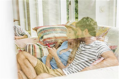 Window view of young couple on living room sofa reading smartphone texts Stock Photo - Premium Royalty-Free, Code: 649-08060744