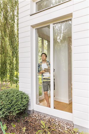 Young man leaning against and looking out of house window Stock Photo - Premium Royalty-Free, Code: 649-08060747