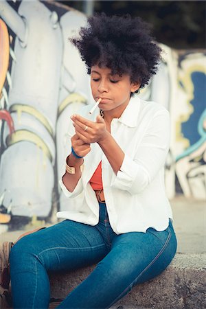 simsearch:649-08060336,k - Young woman igniting cigarette in front of graffiti wall Stock Photo - Premium Royalty-Free, Code: 649-08060784