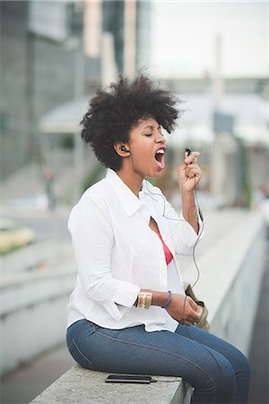 simsearch:6108-06167284,k - Young woman singing into earphone whilst sitting on shopping center wall Foto de stock - Sin royalties Premium, Código: 649-08060811