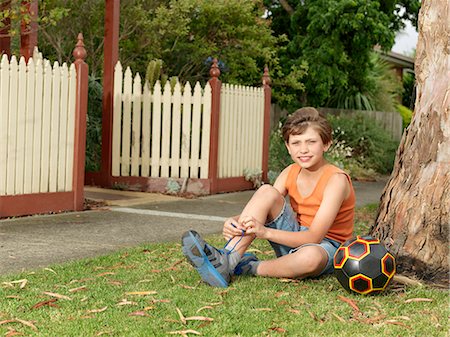 soccer shorts for boys - Portrait of boy with soccer ball sitting on grass tying trainer laces Stock Photo - Premium Royalty-Free, Code: 649-08060813