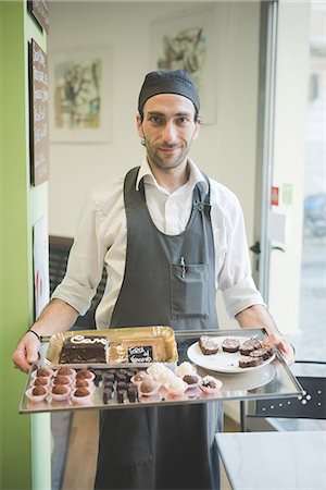 simsearch:649-08084554,k - Waiter carrying tray of cakes and cookies in cafe Fotografie stock - Premium Royalty-Free, Codice: 649-08084562