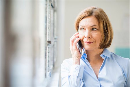 phone female office worker - Mature businesswoman looking out of office window and chatting on smartphone Stock Photo - Premium Royalty-Free, Code: 649-08084889