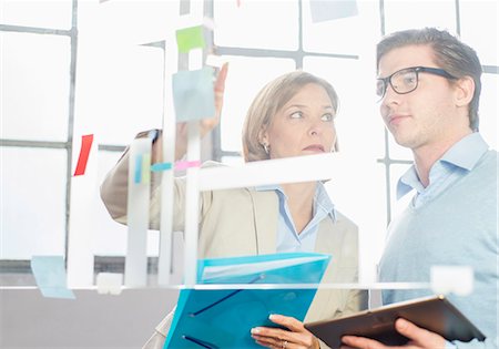 Businessman and woman pointing at idea notes on office glass wall Stock Photo - Premium Royalty-Free, Code: 649-08084897