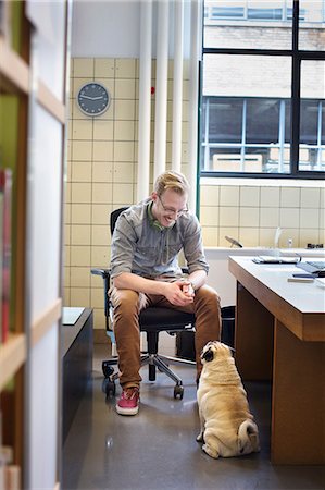 Young man looking down at cute dog from office desk Stock Photo - Premium Royalty-Free, Code: 649-08084982