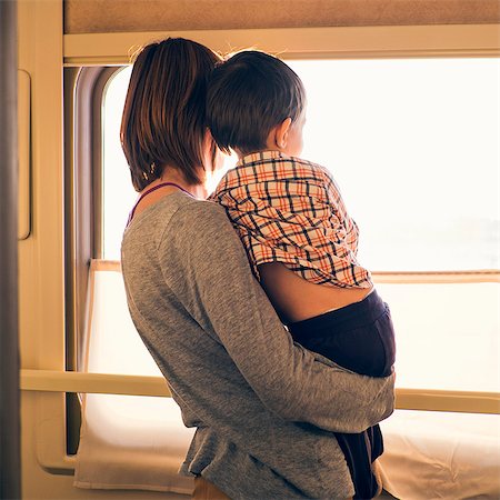 Rear view of woman and toddler son looking out of sunlit train window Stock Photo - Premium Royalty-Free, Code: 649-08085147