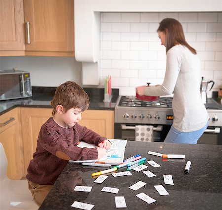 Boy coloring in book on kitchen counter as mother prepares dinner Photographie de stock - Premium Libres de Droits, Code: 649-08085995
