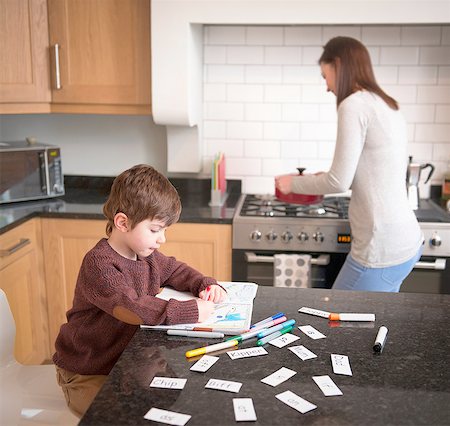 family playing in the kitchen - Boy coloring in book on kitchen counter as mother prepares dinner Stock Photo - Premium Royalty-Free, Code: 649-08085995