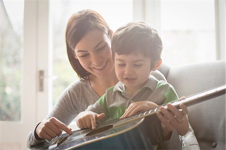 family sitting in couch - Boy sitting on mother's lap and learning to play guitar Stock Photo - Premium Royalty-Free, Code: 649-08085991