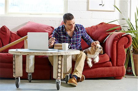 people sitting on a sofa - Mid adult man writing address on parcels whilst petting dog in picture framers Stock Photo - Premium Royalty-Free, Code: 649-08086938