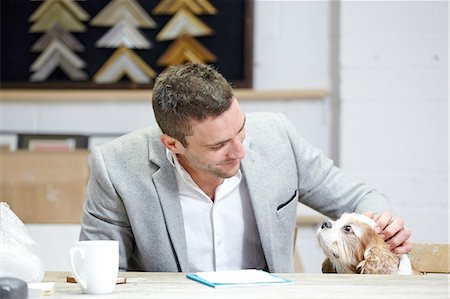 Mid adult man petting dog at desk in picture framers workshop Foto de stock - Royalty Free Premium, Número: 649-08086956