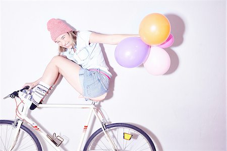 Studio shot of young woman with feet up on bicycle holding bunch of balloons Photographie de stock - Premium Libres de Droits, Code: 649-08117845